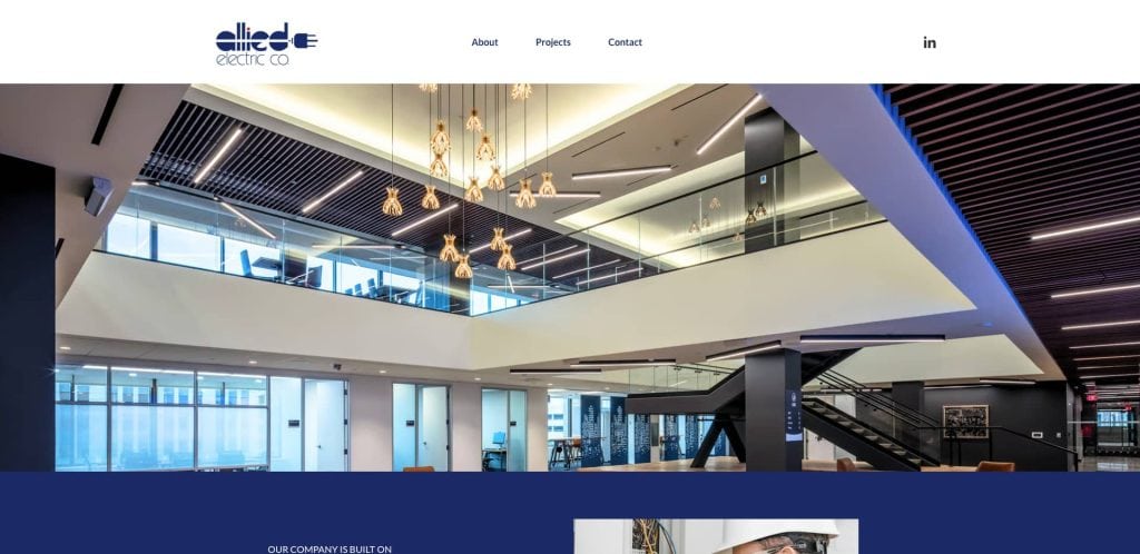 Modern office interior with large open lobby, glass railings on upper floor, geometric ceiling lights, and a staircase. Allied Electric Co logo and navigation bar are visible at the top of the website.