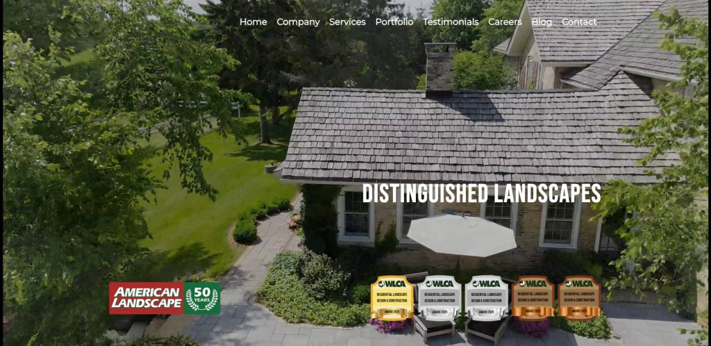 Aerial view of a landscaped home with stone patio, umbrella, and lush green lawn. Text reads Distingushed Landscapes. Four award badges and an American Landscape 50-year logo appear at the bottom left.