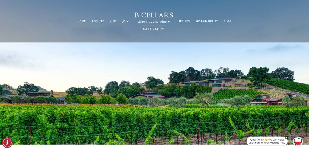 Vineyards with rows of grapevines stretch across rolling hills, with buildings nestled among trees in the background under a clear sky. The B Cellars winery website navigation is visible at the top.