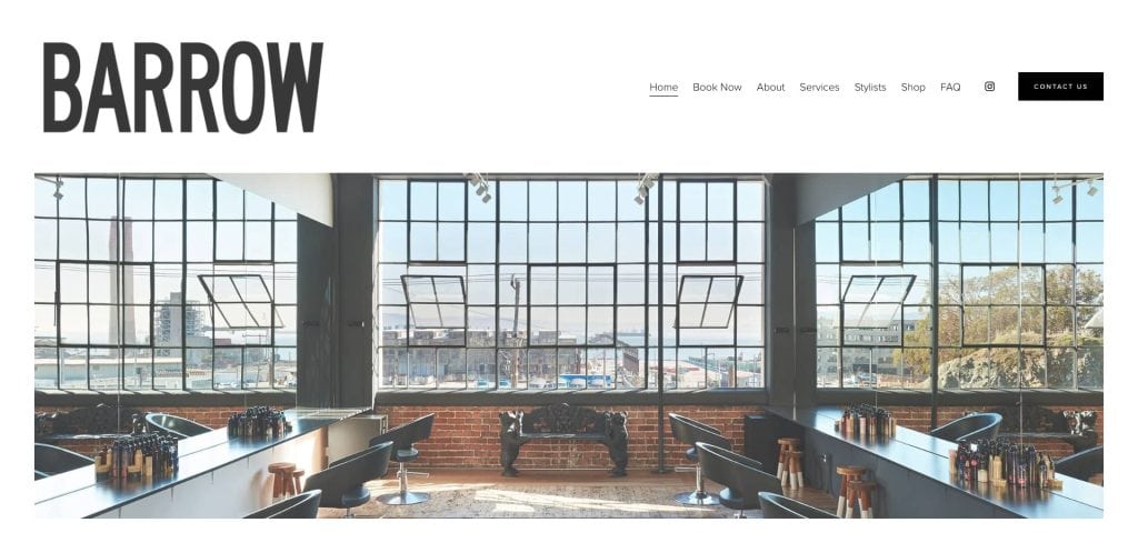 Modern hair salon interior with large windows, black styling chairs, mirrors, and hair products on countertops. Cityscape and blue sky visible through windows. BARROW logo and website navigation are at the top.