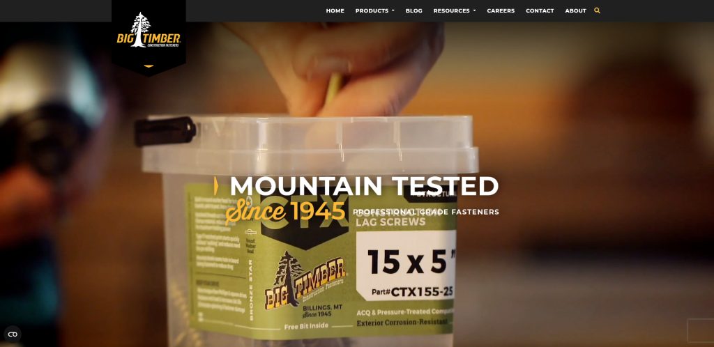 A close-up of a hand reaching into a container of Big Timber 15x5-inch professional lag screws, with the text Mountain Tested Since 1945 overlaid on the image.