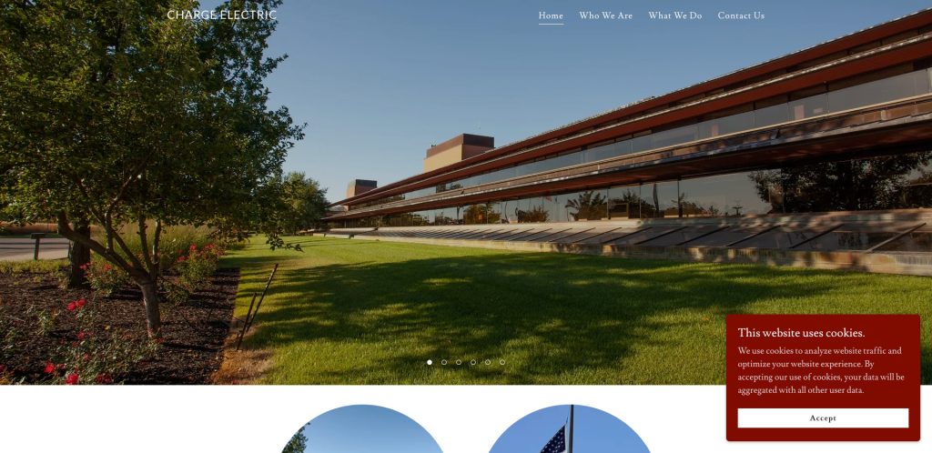 Modern glass office building with a slanted facade and manicured green lawn under a clear blue sky; navigation menu and cookie consent popup visible on the website.