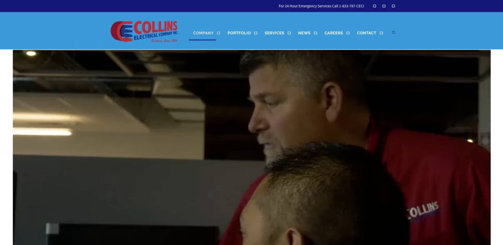 Two men in red Collins Electrical Group shirts are standing and looking in the same direction inside an office, with the company’s website header visible at the top.