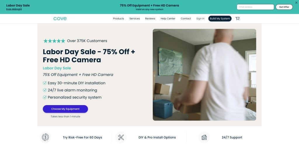 A person carries a box into a living room. The website banner advertises a Labor Day Sale: 75% off equipment plus a free HD camera, with features like DIY installation and 24/7 monitoring for a security system.