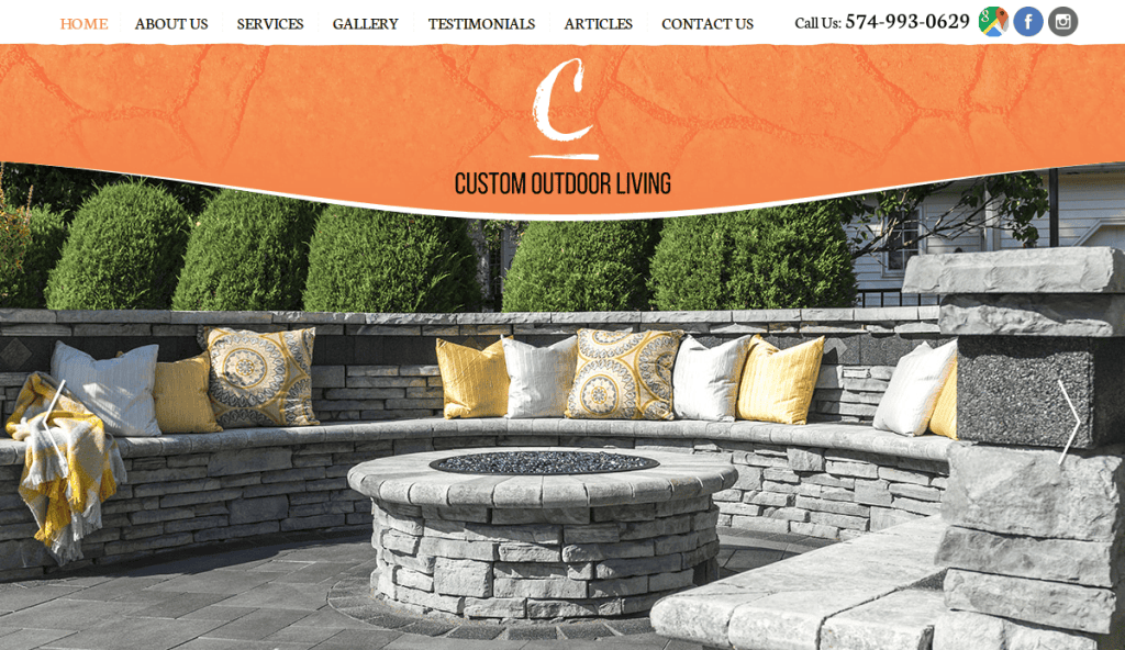 A curved stone outdoor seating area with gray and yellow pillows, surrounded by greenery, featured on the Custom Outdoor Living website header. Contact info and navigation menu are displayed at the top.
