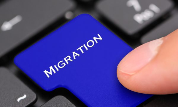 A finger presses a blue keyboard key labeled MIGRATION, replacing a standard key on a black computer keyboard—symbolizing moving a Website from WordPress or another Proprietary CMS.