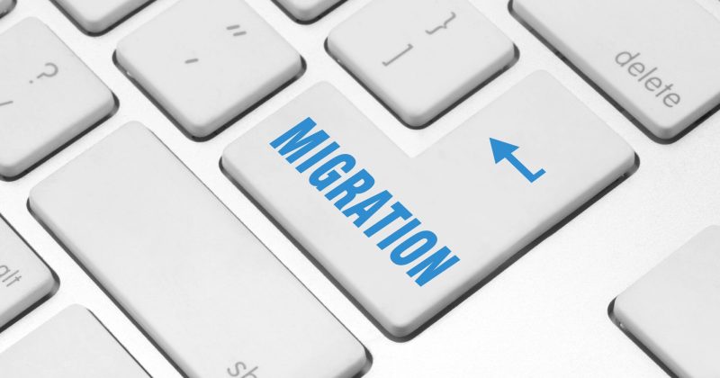 A white computer keyboard with a large Enter key labeled MIGRATION in blue text and an arrow, symbolizing the concept of WordPress Migration or upgrading from an outdated migration process.