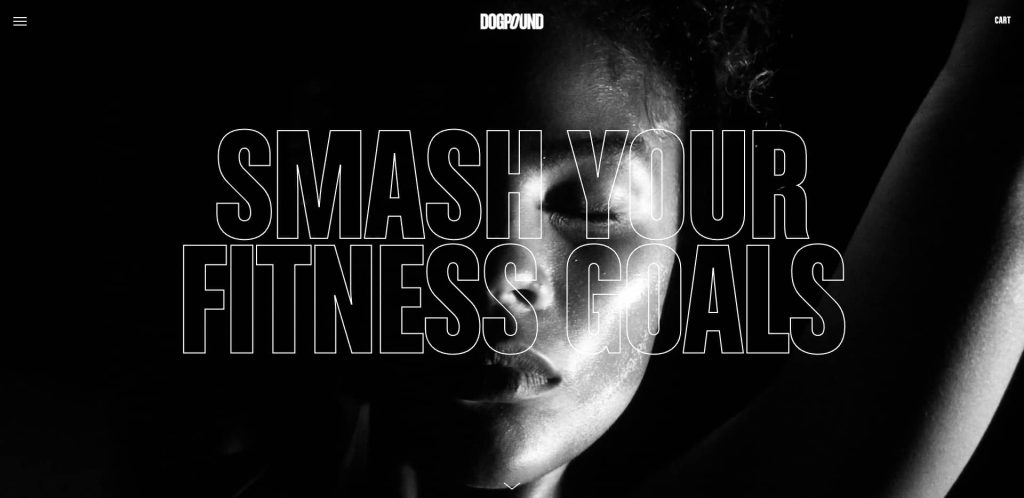 Black and white close-up of a person’s face with bold, transparent text overlay reading “SMASH YOUR FITNESS GOALS.” The lighting highlights half of the face, creating a dramatic effect. The Dogpound logo appears at the top.