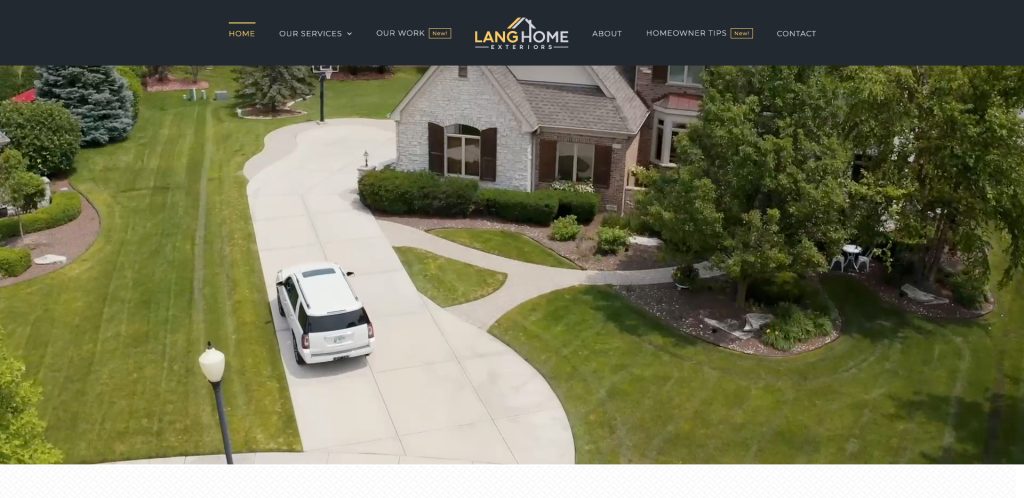 A white SUV drives up a curved concrete driveway toward a brick house with a well-maintained yard, green grass, shrubs, and mature trees. The scene appears to be from a website for a home exterior company.