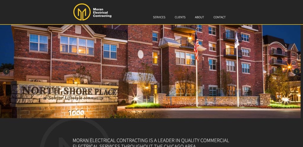 Website homepage for Moran Electrical Contracting featuring a photo of a brick building with lit windows, American flags, and a sign reading “North Shore Place.” The company logo and navigation menu appear at the top.