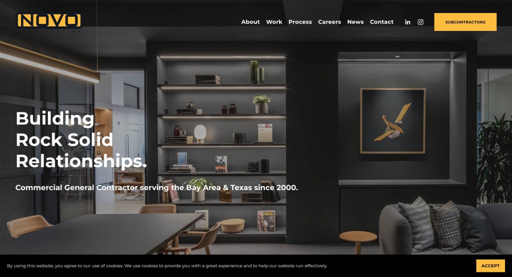 Modern office interior with a gray color scheme, shelves with books and decor, a table with chairs, framed art of a bird on the wall, and text promoting a general contractor company.
