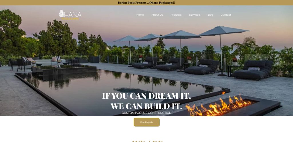 A luxurious outdoor pool area with lounge chairs, umbrellas, and a modern fire pit surrounded by greenery. Text overlay reads, IF YOU CAN DREAM IT, WE CAN BUILD IT. CUSTOM POOLS & CONSTRUCTION.