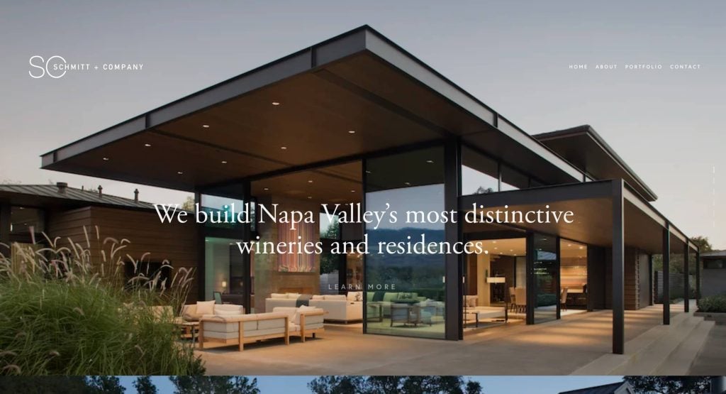 A modern glass and steel building with outdoor seating, illuminated at dusk. Overlaid text reads: We build Napa Valley’s most distinctive wineries and residences. Website menu options appear at the top.