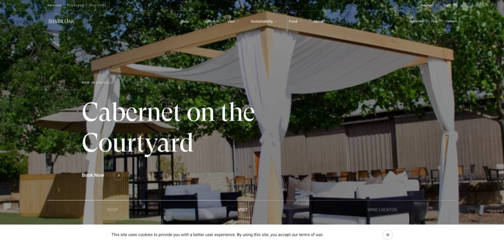 An outdoor seating area with a wooden pergola draped in white fabric, surrounded by trees and patio furniture. Text overlay reads Cabernet on the Courtyard.