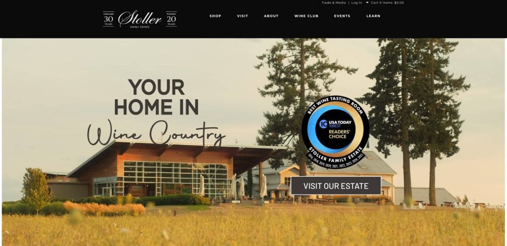 A modern building with large windows stands in a grassy field, with trees and another house in the background. Text reads “Your Home in Wine Country” and a badge highlights a USA Today Readers’ Choice award.