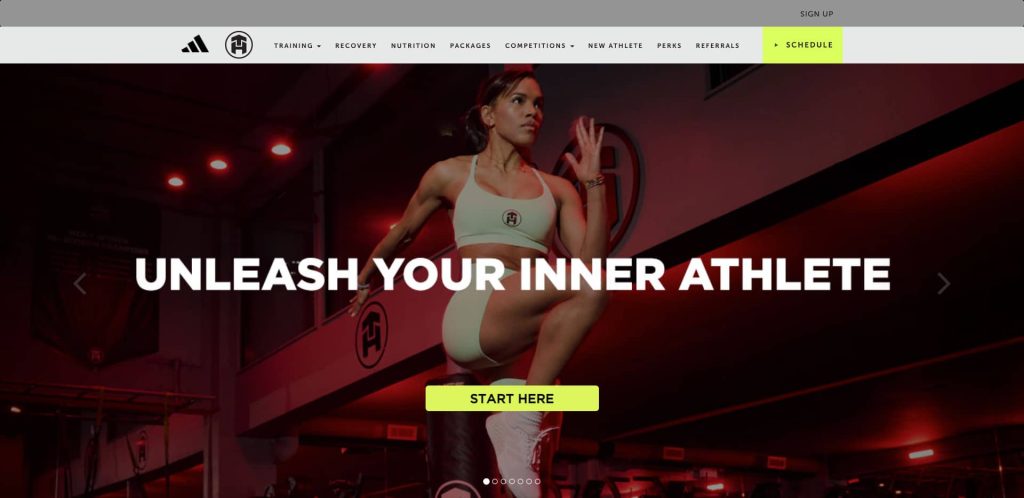 A fit woman in athletic wear performs a high knee exercise in a gym with red lighting. Large white text reads Unleash Your Inner Athlete, and a yellow Start Here button is below. Navigation menus appear at the top.