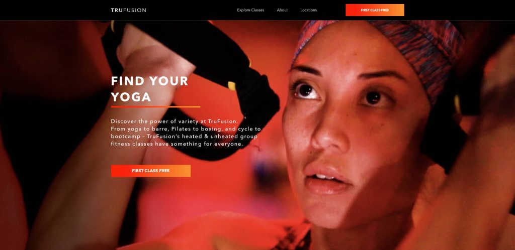 A focused woman in athletic wear holds resistance straps during a fitness class at TruFusion. The text beside her reads, Find Your Yoga, promoting group fitness classes and a free first class offer.