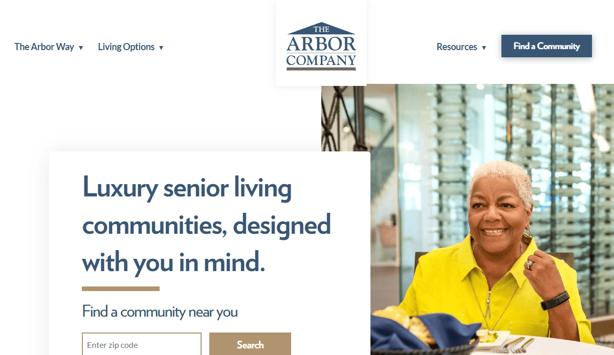 A smiling older woman with silver hair enjoys a meal at a bright senior living community. The website header reads “The Arbor Company” and features an Assisted Living Website Design with a search for senior communities.
