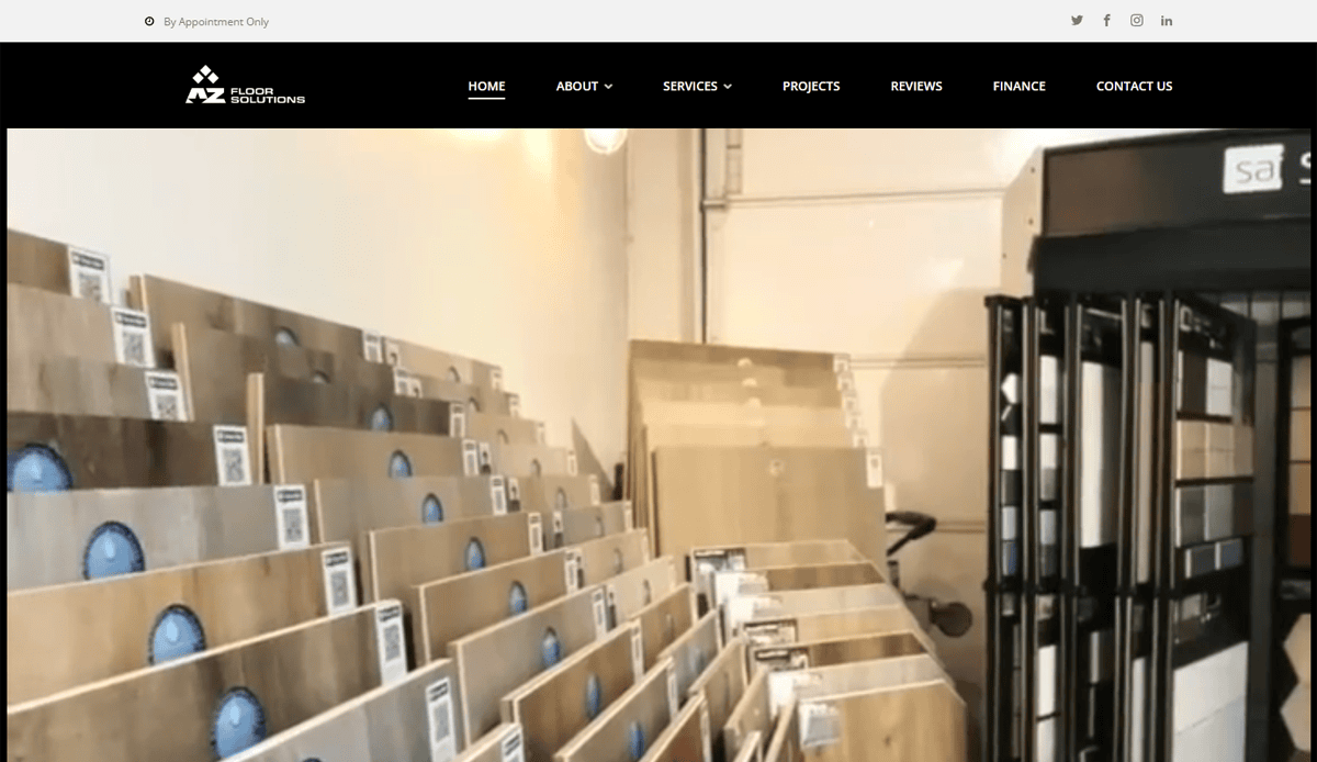 Display of assorted flooring samples arranged upright in rows inside a showroom, with a black sign and navigation menu visible at the top, showcasing tile contractor website design focused on performance and lead generation.