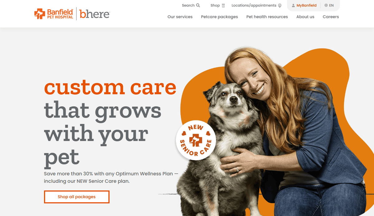A smiling woman with long red hair hugs a gray and white dog. Text reads: “custom care that grows with your pet,” promoting Banfield Pet Hospital’s new senior care plan on their professional veterinary website, with navigation links and an orange “Shop all packages” button.