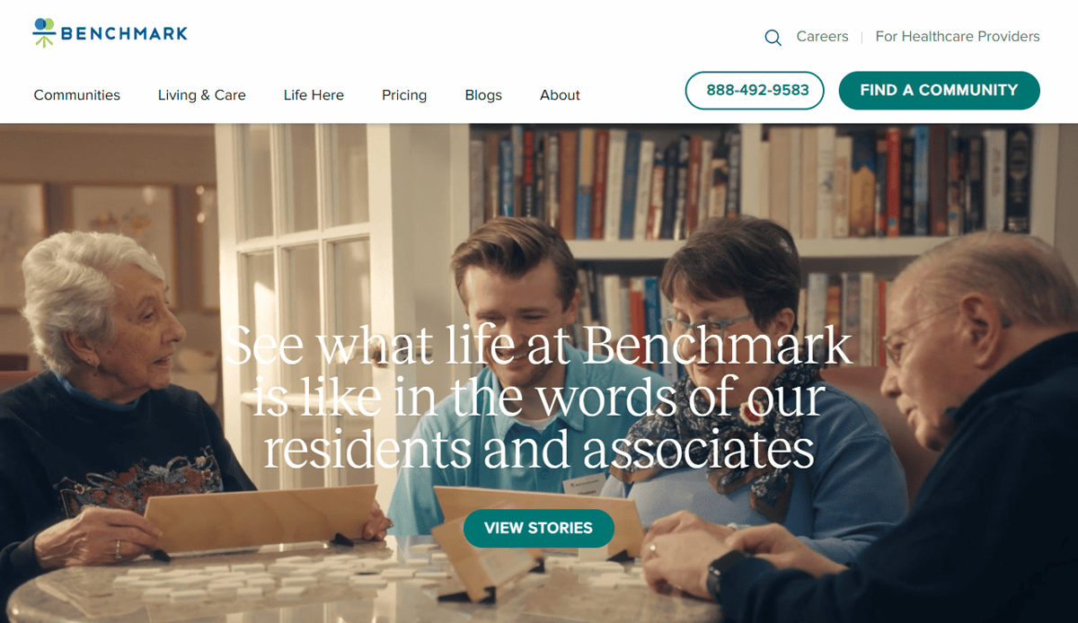 Four seniors sit at a table smiling and playing a board game together in a cozy, well-lit room with shelves of books in the background. Text overlay highlights stories from residents and associates featured on our Assisted Living Website.