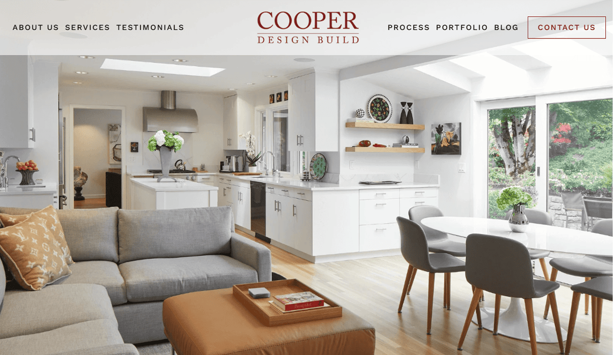 Modern open-concept kitchen and living room, perfect for a Professional Construction Website, featuring white cabinets, stainless steel appliances, a cozy grey sofa, round dining table with grey chairs, and large glass doors overlooking a green garden.