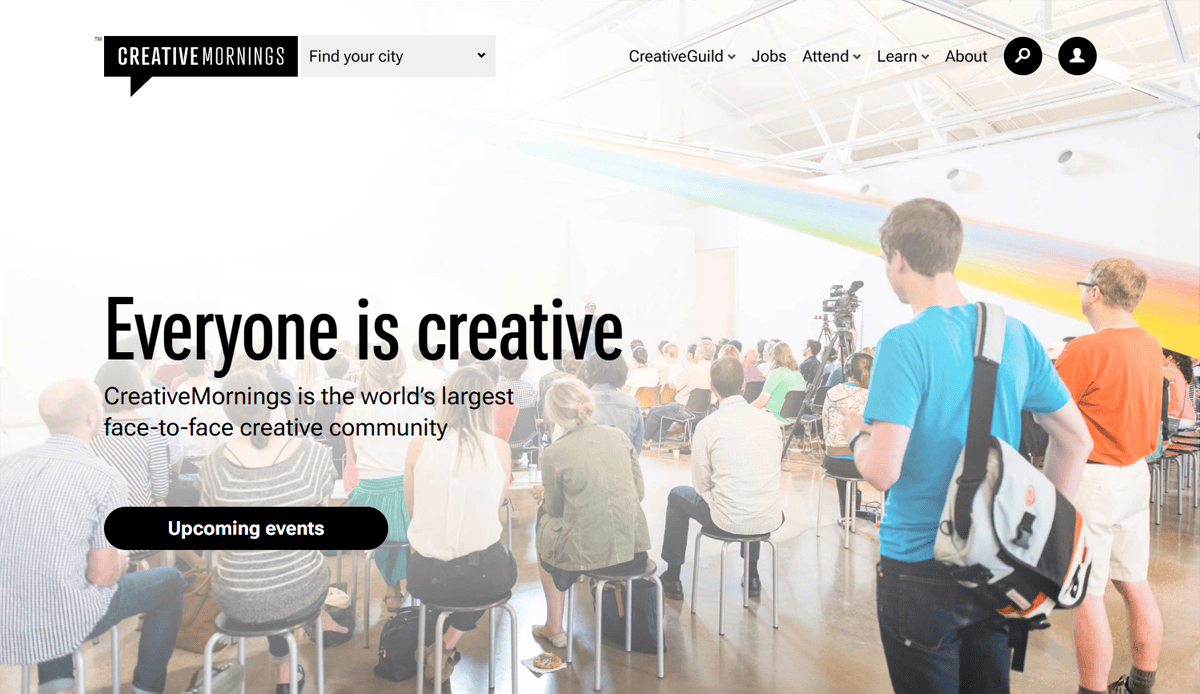 A diverse group of people sit on chairs in a bright, modern space with a rainbow installation overhead, attending a CreativeMornings event. Large text reads Everyone is creative—perfect inspiration for event website design.