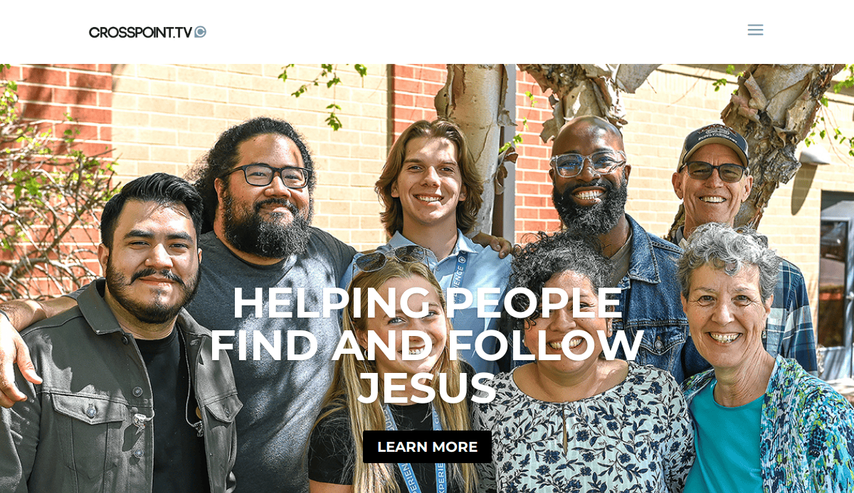 A diverse group of eight smiling people stand together outdoors in front of a brick wall and leafy tree, showcasing a welcoming homepage. Overlaid text reads “HELPING PEOPLE FIND AND FOLLOW JESUS” with a “LEARN MORE” button below.