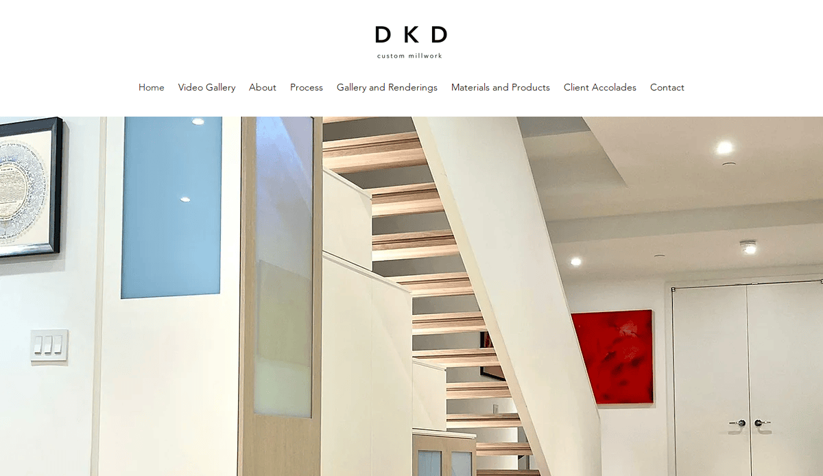 Modern interior with a light wood staircase featuring open risers and glass panels. White walls, contemporary art, and sleek cabinetry by expert cabinet makers complete the minimalist design. “DKD custom millwork” is displayed at the top.