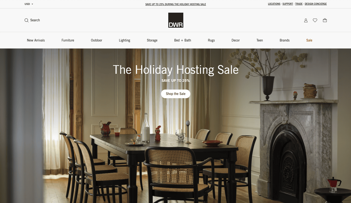 A modern dining room with a dark wood table, six cane chairs, a fireplace, and decorative branches is showcased on a furniture website design promoting The Holiday Hosting Sale.