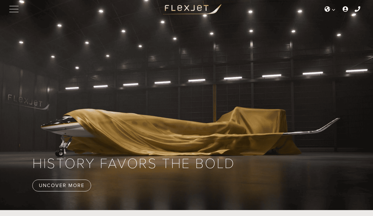 A private jet partially covered by a gold cloth sits in a dimly lit digital hangar with “FLEXJET” branding and the words “HISTORY FAVORS THE BOLD” displayed above a button labeled “UNCOVER MORE.”.