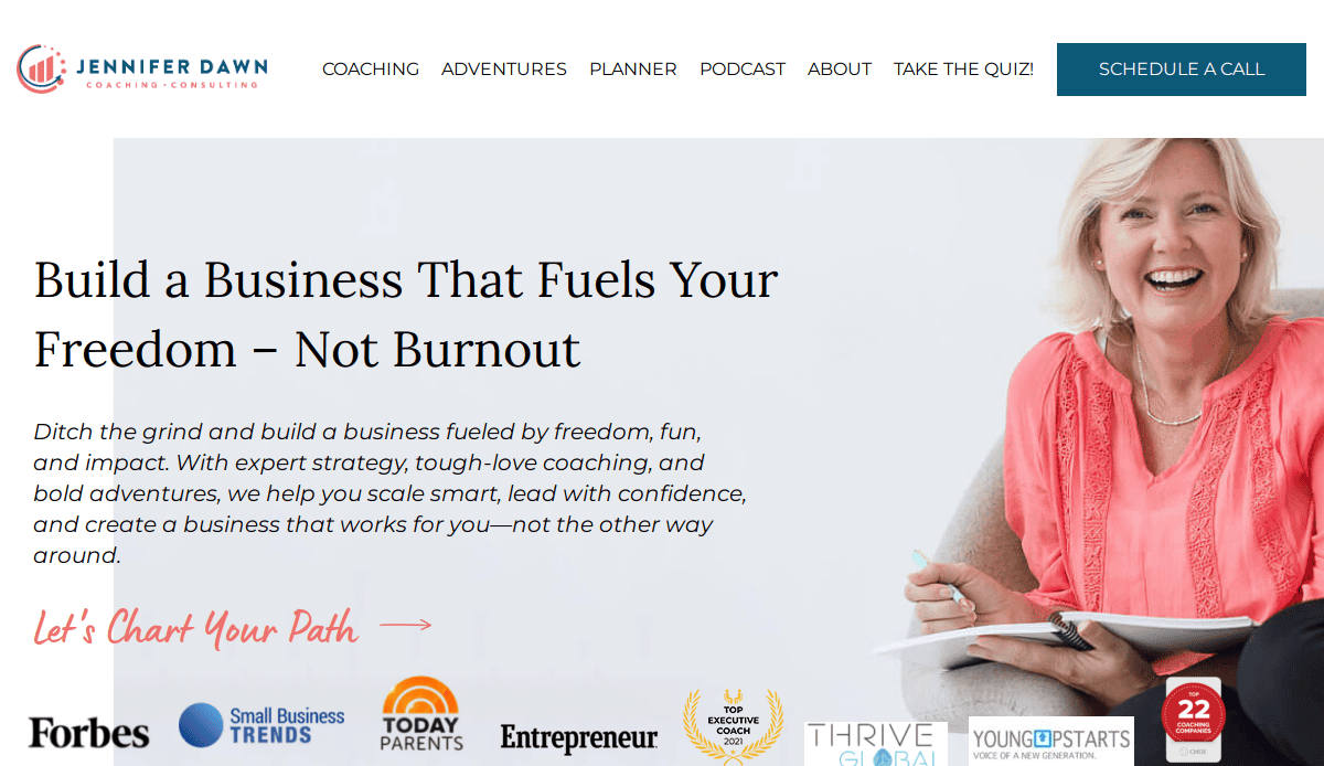 A smiling woman sits with a notebook in hand. The website headline reads, Build a Business That Fuels Your Freedom – Not Burnout. Explore how to plan with purpose and build a coaching website. Media logos and navigation appear at the top.