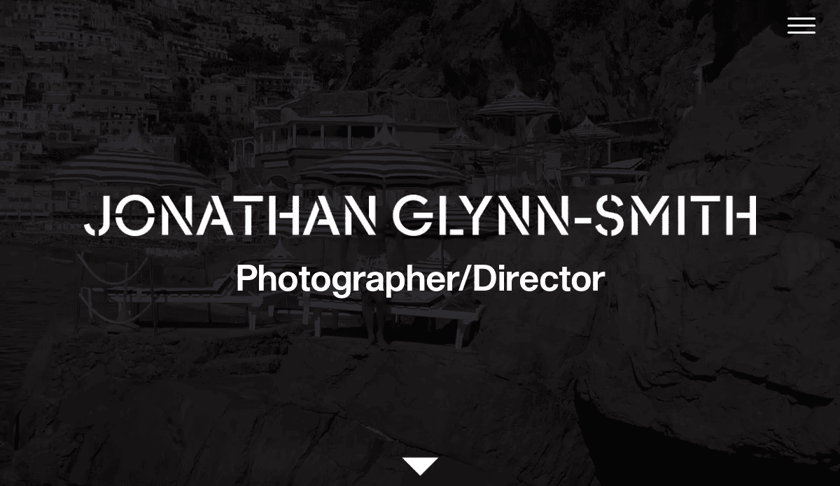 Text JONATHAN GLYNN-SMITH Photographer/Director appears over a rocky coastal background with buildings perched on cliffs, evoking the elegance and creativity found in artisan website design.