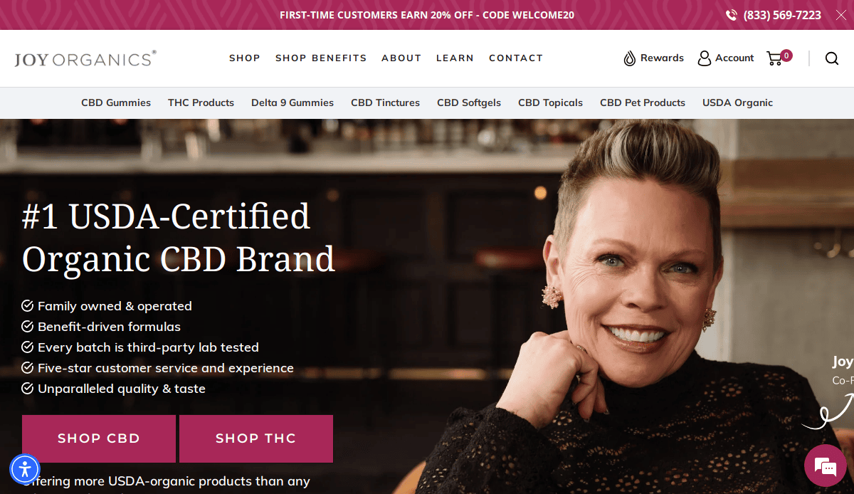 A smiling person with short hair and earrings sits in a modern setting. The Joy Organics CBD website design promotes USDA-Certified Organic products, featuring navigation links and special offers for their compliant CBD business at the top.