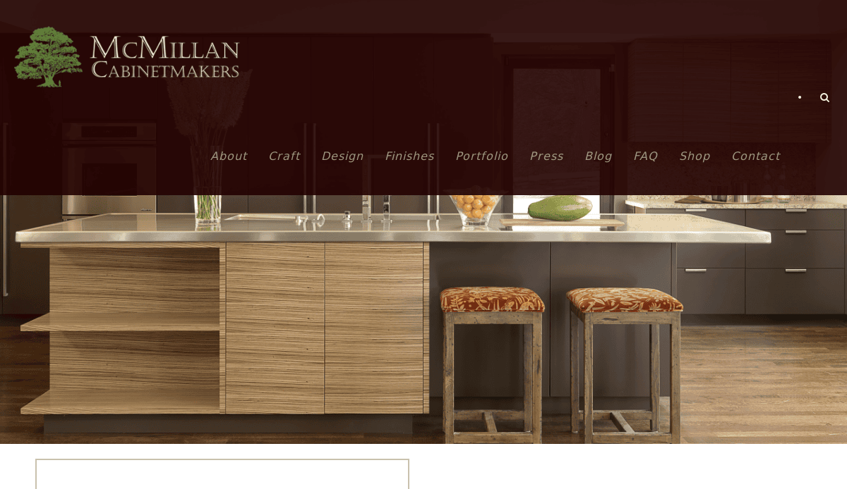 Modern kitchen with wood cabinets, a light stone island countertop, two patterned stools, and fruit on the counter; McMillan Cabinetmakers logo and website design navigation menu overlay the top of the image.