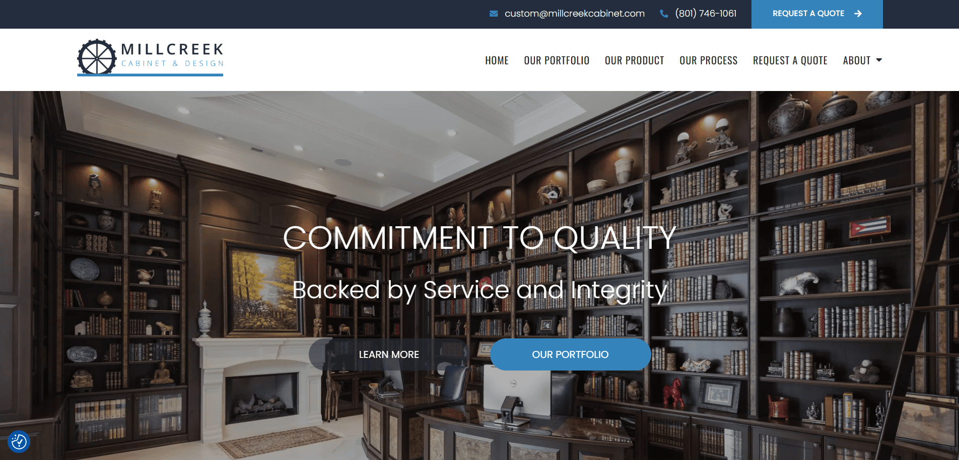 Elegant home office with dark wood built-in bookshelves by expert cabinet makers, a fireplace, chandelier, large desk, and upholstered chair. The website banner displays Millcreek Cabinet & Design and navigation menu at the top.