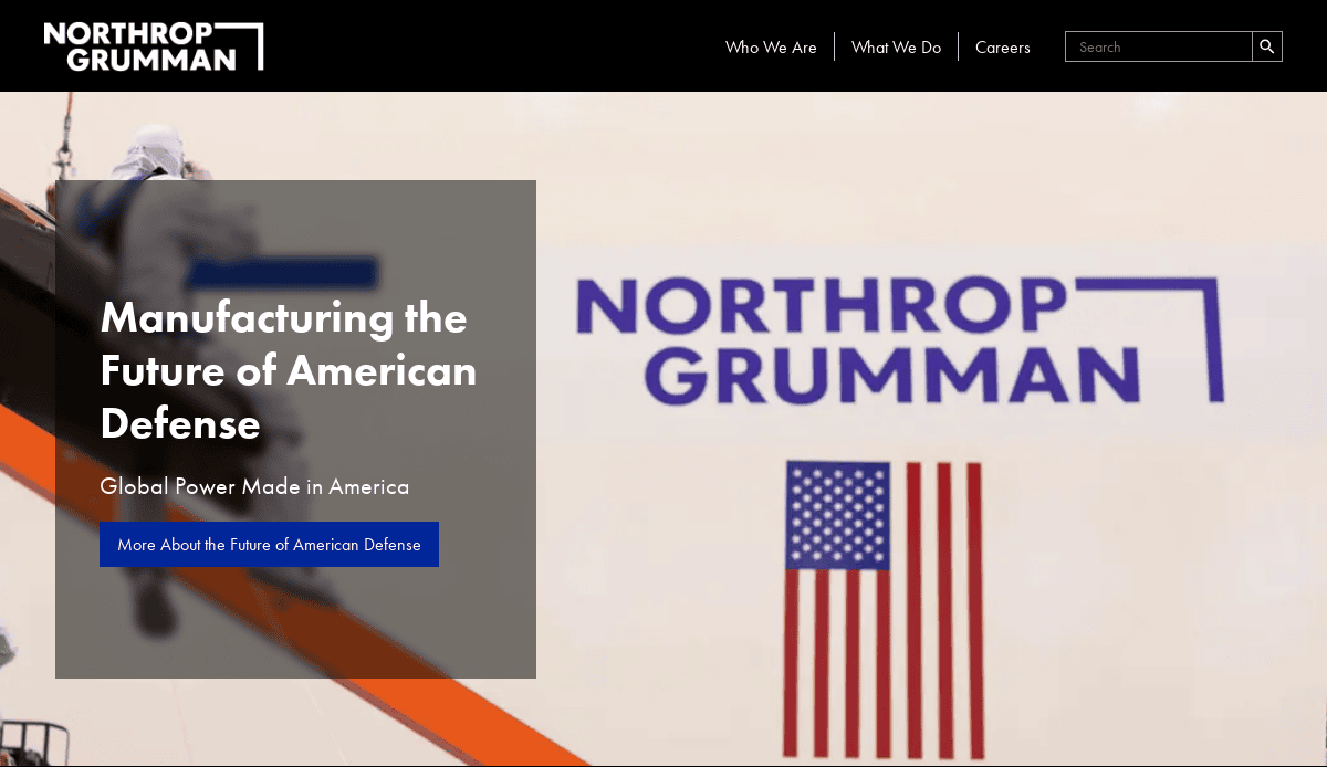 A person in safety gear stands near a large sign displaying the Northrop Grumman logo and an American flag. Text reads, Manufacturing the Future of American Defense. Explore digital hangar innovations—global power made in America.
