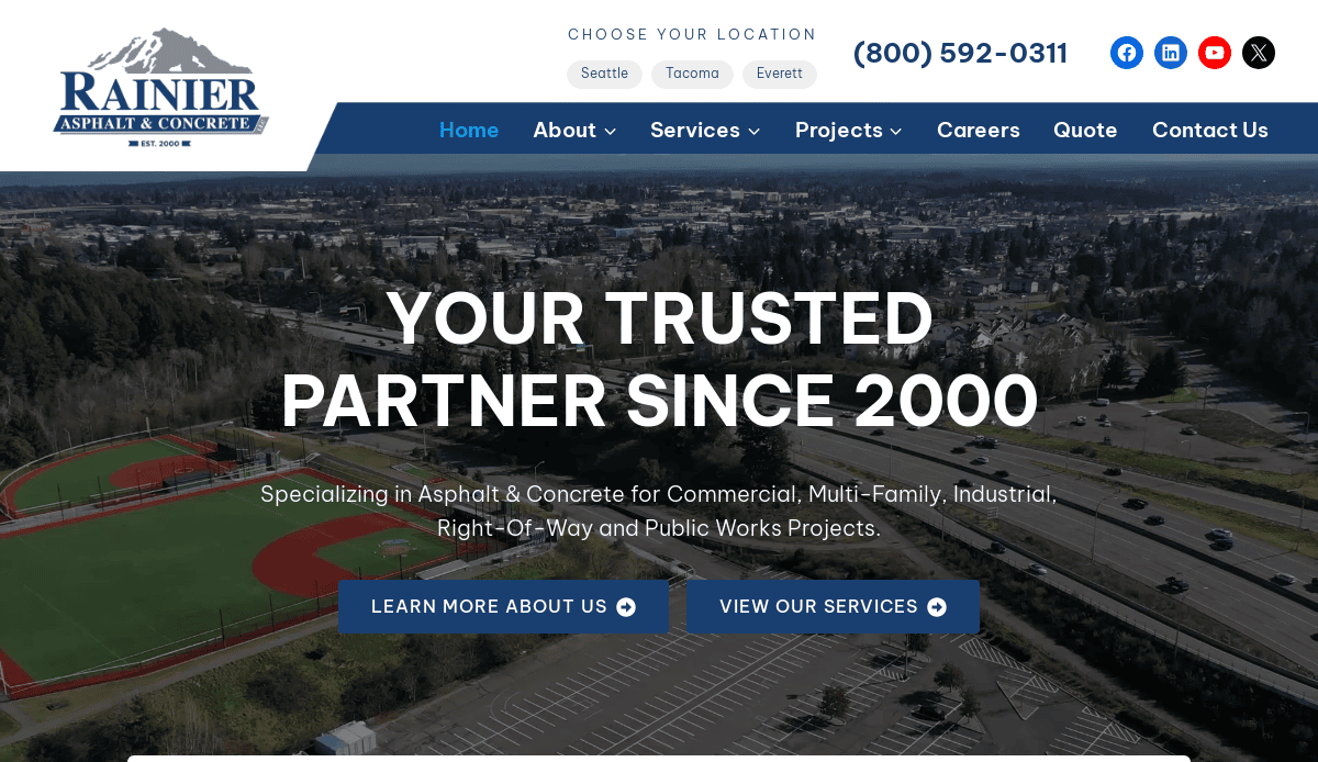Screenshot of Rainier Asphalt & Concrete’s website homepage, featuring a cityscape background, company logo, contact number, navigation menu, and headline: “Your Trusted Partner Since 2000.” Showcases effective website design for an asphalt contractor.