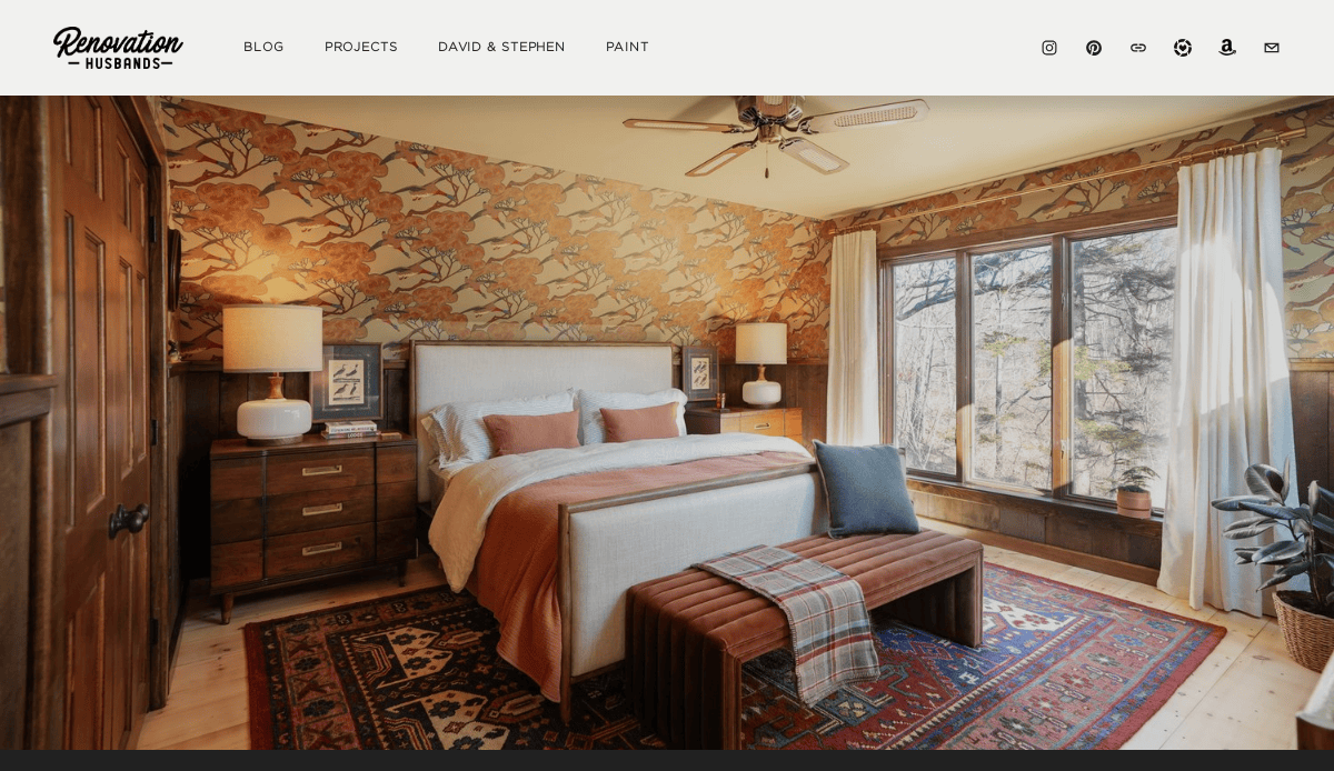 A cozy bedroom with a king bed, wood furniture, orange and beige bedding, patterned wallpaper, large windows, and a Persian rug. Natural light fills the room—ideal inspiration for website design aiming to convert visitors with inviting visuals.