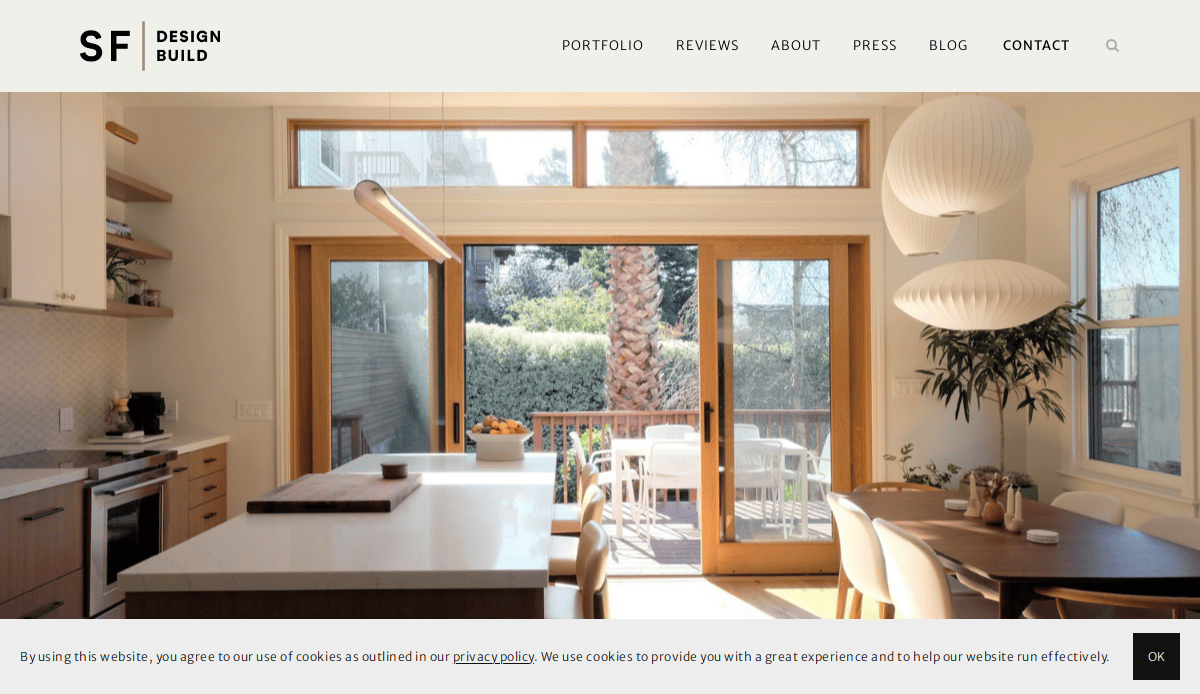 A modern kitchen and dining area with large glass doors opening to a sunny wooden deck and green backyard, featuring light wood cabinetry, a dining table, pendant lamps, and subtle website design touches that help convert visitors.