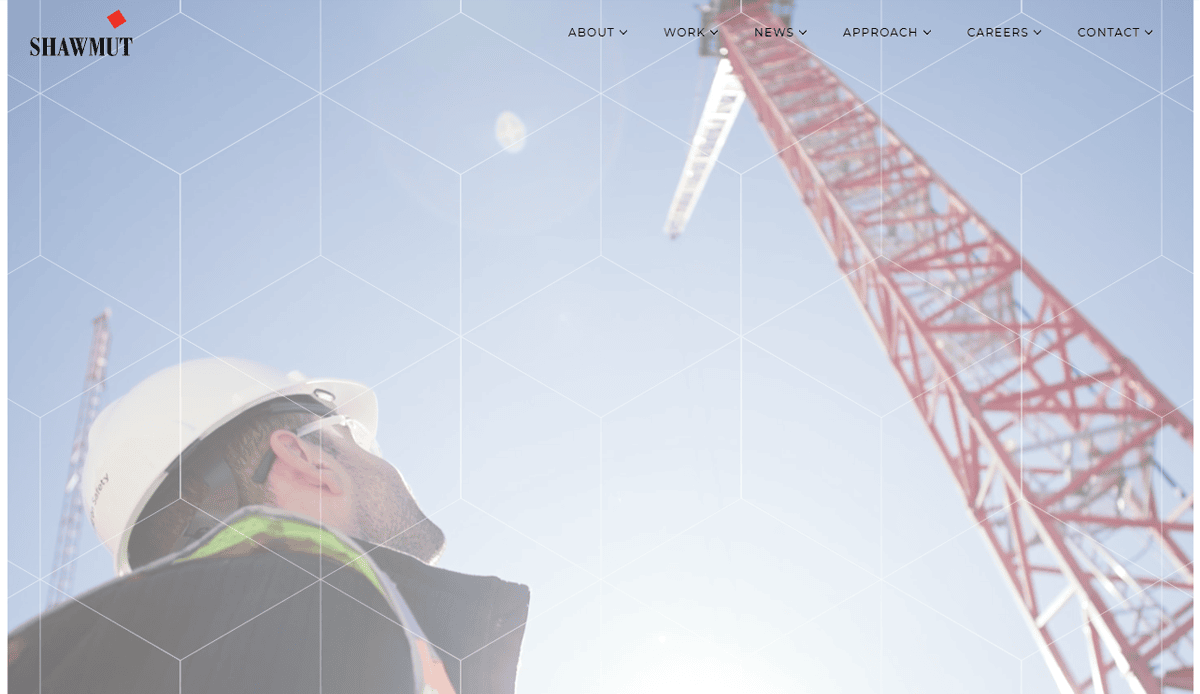 A construction worker in a hard hat and safety vest looks up at a tall red crane under a bright sky, highlighting the Shawmut logo and website navigation—an impressive example of professional construction website design.