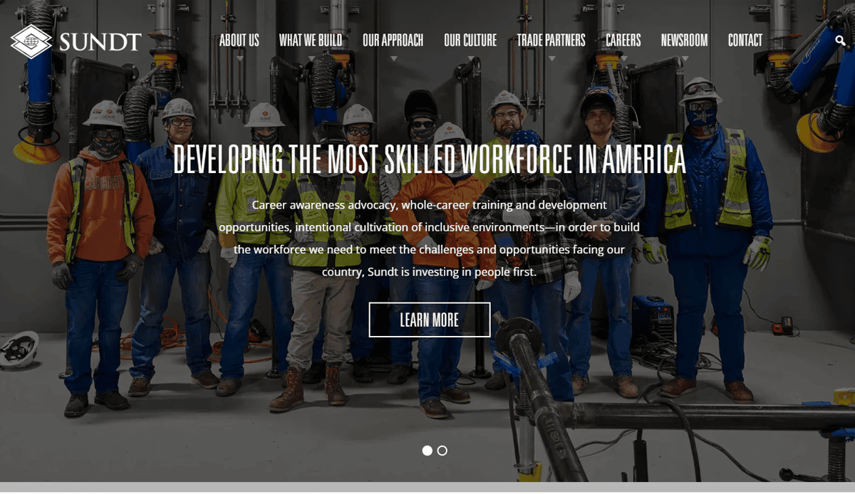 A group of professional construction workers in safety gear stands at a commercial construction site. Text overlay reads, “Developing the most skilled workforce in America.” Explore career opportunities and website design with Sundt. “Learn More” button and Sundt logo shown.