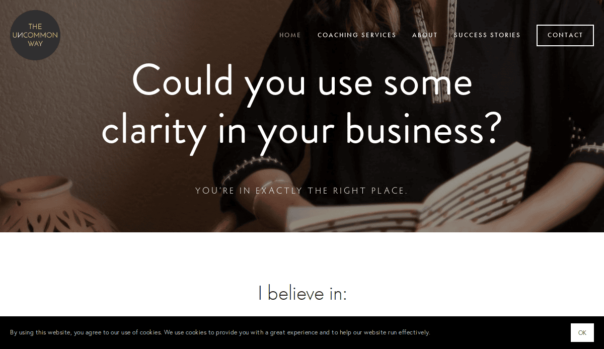 A coaching website homepage with a dark overlay shows a woman holding a notebook. Large text reads, Could you use some clarity in your business? Plan with purpose, with navigation links and a cookie consent banner visible.