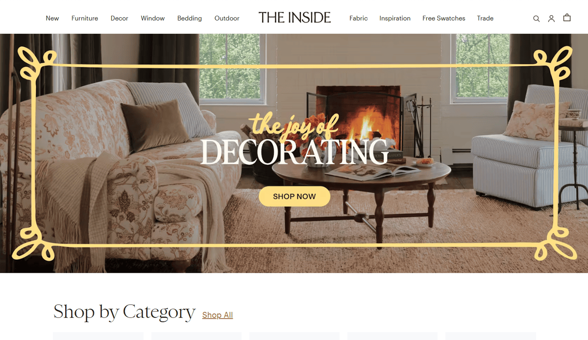 A cozy living room with a floral sofa, patterned armchair, coffee table, and fireplace highlights beautiful Furniture Website Design, overlaid with text reading the joy of DECORATING and a yellow Shop Now button.