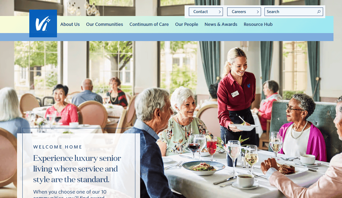A cheerful server brings food to a table of smiling senior residents dining together in a bright, elegant restaurant featured on an Assisted Living Website, complete with large windows and inviting ambiance.