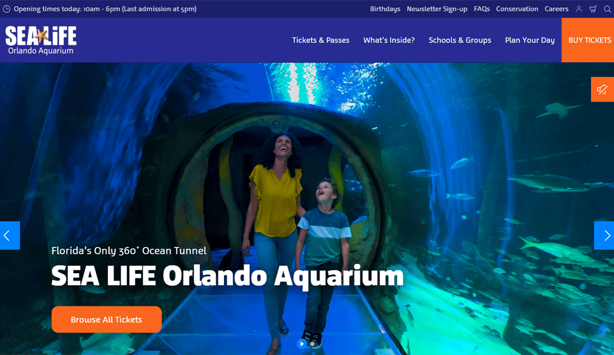 A woman and a boy walk through a glass tunnel surrounded by water and fish at SEA LIFE Orlando Aquarium, with aquarium website design featuring easy navigation at the top and a button prompting to browse tickets.