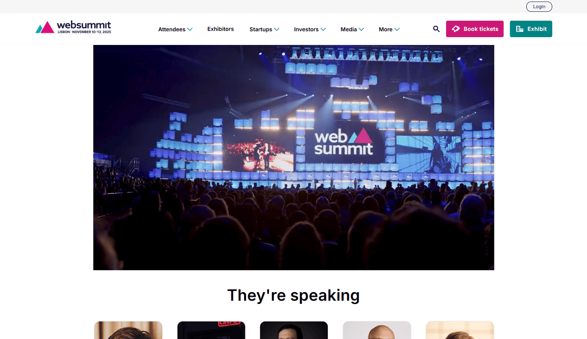 Audience watches a large stage at Web Summit conference, with bright lights and the web summit logo displayed on digital screens, reflecting modern conference website design. Website navigation and event info are visible at the top.