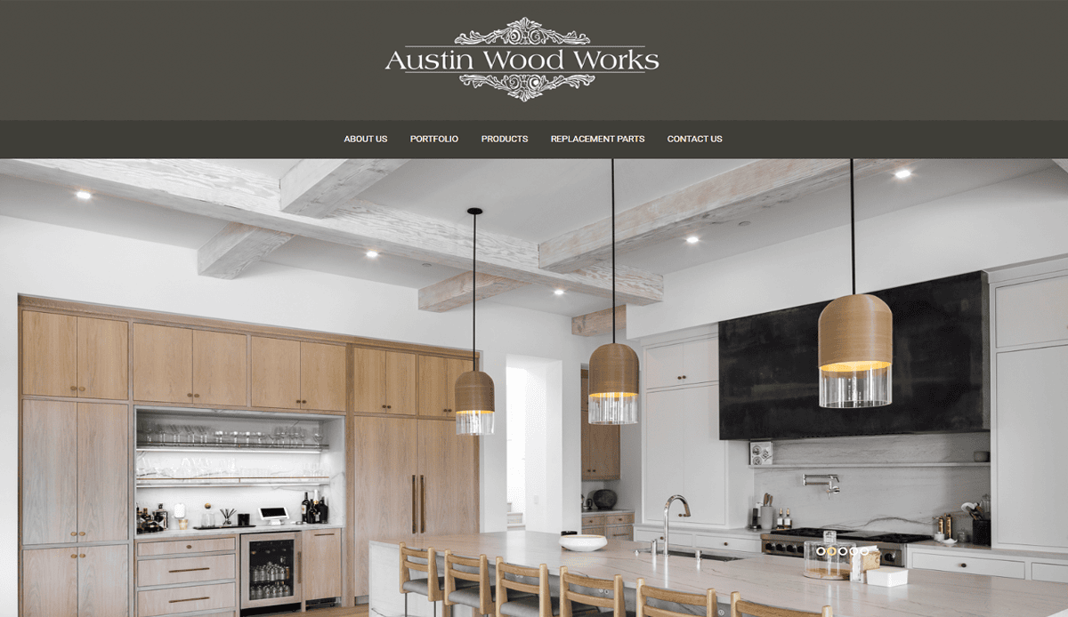 A modern kitchen with light wood cabinets, an island with wooden stools, pendant lights, and a black range hood—an inspiring showcase of website design for carpenters—featured on the Austin Wood Works website.