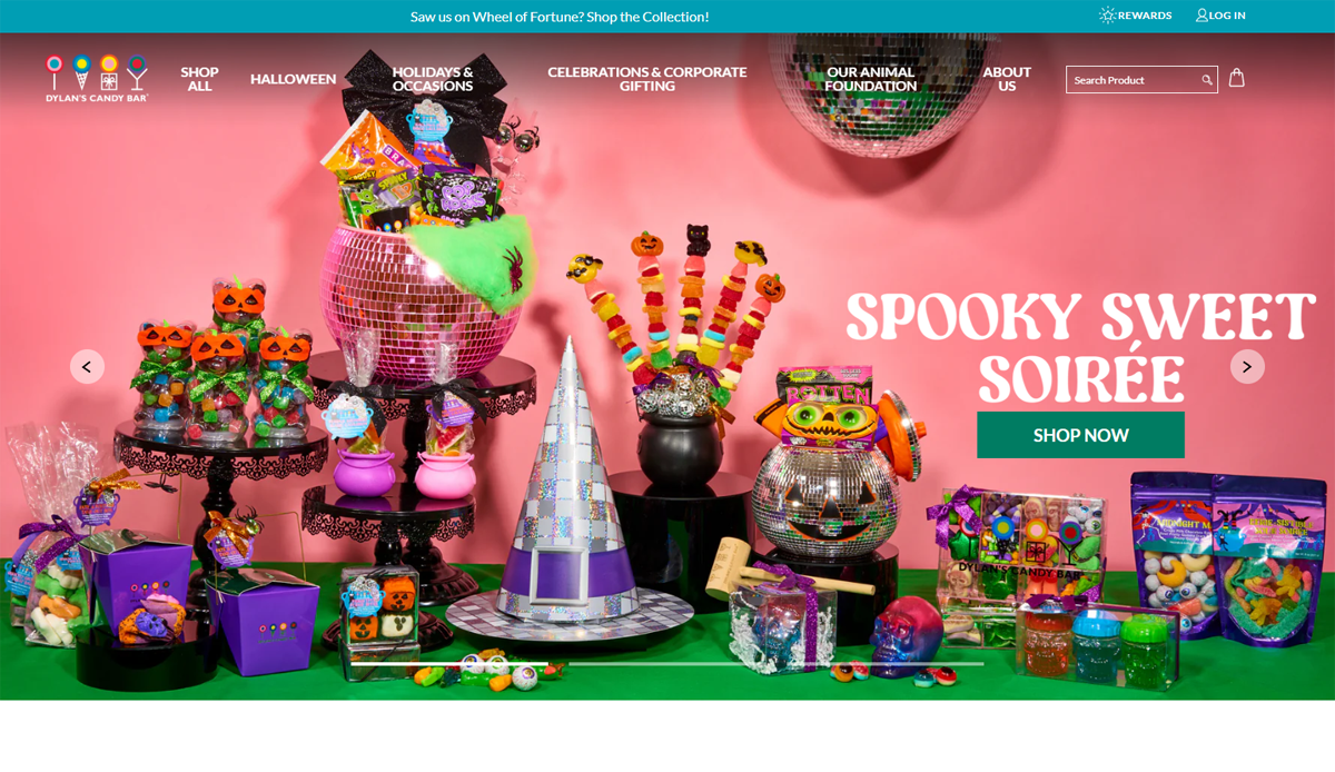 Colorful Halloween-themed candy display with pumpkins, witch hats, and festive gift baskets arranged on shelves and tables against a pink background—perfect inspiration for your candy website design to elevate your online presence. Banner text reads “Spooky Sweet Soirée.”.
