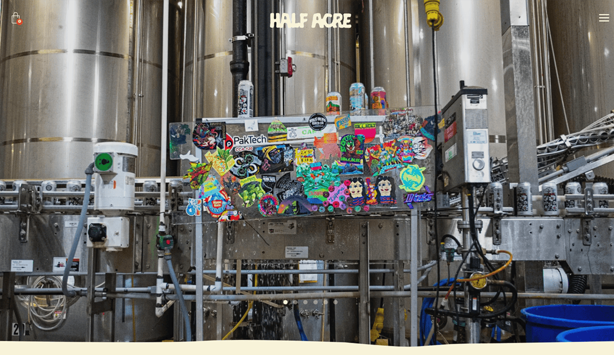 Colorful sticker-covered control panel in an industrial brewery setting, featuring large metal tanks, pipes, and cans; Half Acre logo at the top center—a snapshot perfect for Brewery Website Design showcasing character and modern design trends.